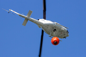 Helicopter with a Bambi bucket filled with water to fight a forest fire