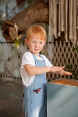 baby with red hair in blue overalls drums on nightstand in boho interior