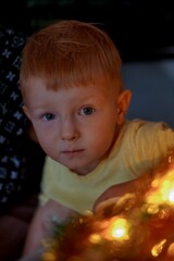 baby with red hair against the background of a Christmas tree looking at the camera