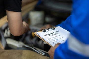Automobile mechanic repairman checking a car engine with inspecting writing to the clipboard the...