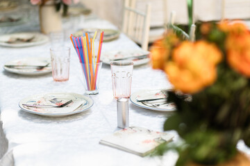 A cheerful outdoor dining setup featuring colorful straws, floral centerpieces, and elegantly arranged plates for a summer gathering