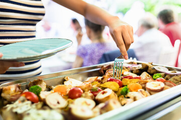 A person serves delicious grilled food at a lively outdoor gathering during a sunny afternoon