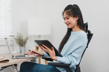 A young woman is working on laptop while using tablet, showcasing modern workspace. Her focused expression reflects productivity and creativity.