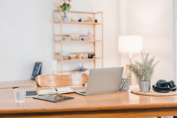 Fototapeta premium A modern workspace featuring laptop, tablet, notebook, and decorative plants, creating serene and productive atmosphere. warm lighting enhances inviting feel of room.