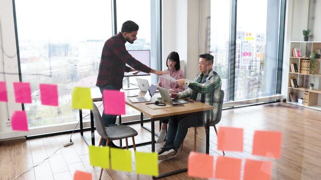 Group of coworkers collaborating in modern office with large windows, surrounded by colorful sticky notes. Active brainstorming session fostering creativity and teamwork.