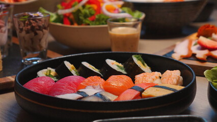 Assorted sushi platter with fresh ingredients on table, accompanied by salads and sauces, perfect for Asian cuisine and gourmet dining. Japanese Food and Culinary Arts