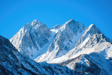 Obraz premium Snow covered mountains rise majestically against clear blue sky, showcasing beauty of natures peaks. crisp air and stunning landscape evoke sense of tranquility and awe