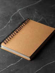 A minimalist brown spiral notebook placed on a dark marble surface, ideal for jotting down notes or creative ideas.