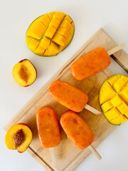 Mango and Peach Popsicles with Stick on Wooden Board Photo