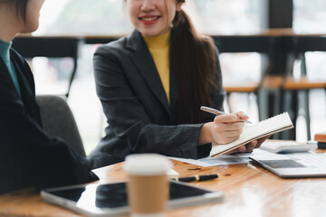 A professional woman engages in discussion while taking notes in notebook.