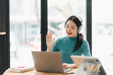 Engaged woman with headphones waving while using laptop in cafe