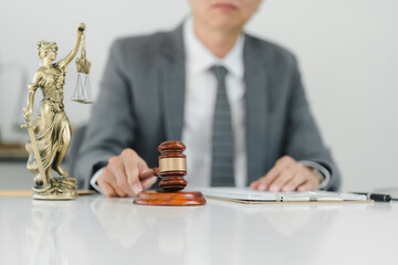 A lawyer in suit is preparing for case with gavel and statue of Lady Justice.