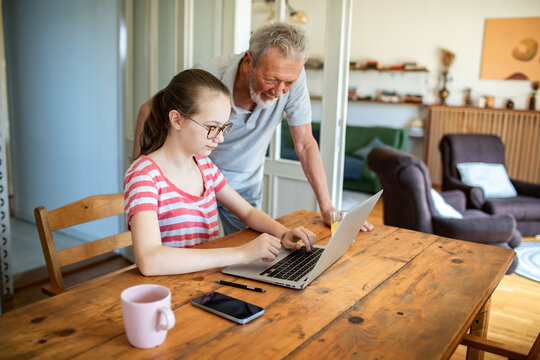 Grandfather helping granddaughter with homework on laptop at home