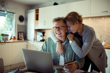 Happy mature couple using credit card on laptop at home