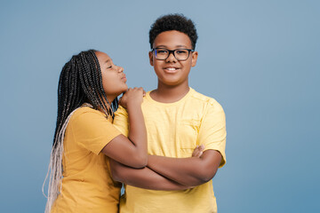 Happy cute sister kissing brother isolated on blue background