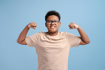 Naklejka premium Portrait of strong African teenager wearing yellow t-shirt showing muscles, biceps