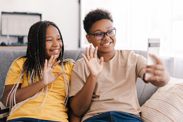 Two smiling kids waving during video call at home