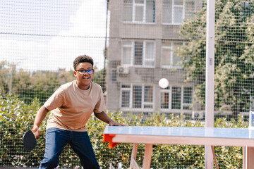 Handsome African American boy playing ping pong outdoors on sunny day