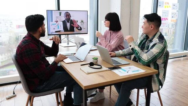 Coworkers collaborating during video conference meeting in modern office setting. Engaged in virtual discussion with remote colleague. Professional teamwork and communication.
