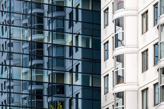 A close-up view of a sleek, curved glass facade of a contemporary high-rise building, showcasing the reflection of another skyscraper with multiple windows and balconies in Rotterdam