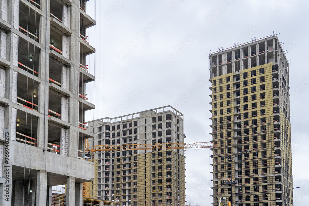Poster three unfinished apartment buildings with scaffolding and windows are being built on a cloudy day