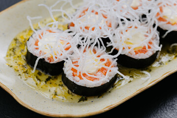 Gourmet sushi rolls topped with crispy rice noodles, salmon, and cream cheese on a decorative plate