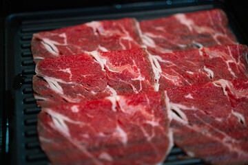 Sliced marbled premium raw beef for BBQ meal is served in the black dish. Food ingredient object, close-up and selective focus.