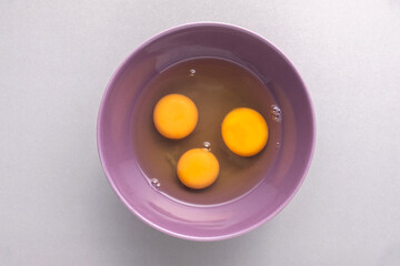 3 raw eggs in purple cup on grey background