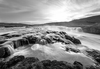 Waterfall panorama near Kaflafell in the south of Iceland with rapids, rocks and strong currents. Melting water from glaciers with midnight sunset at midsummer. Black and white, long time exposure.