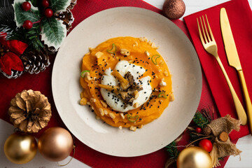 Sweet potato cream with poached egg and mushrooms. Plate on a table with Christmas decoration.