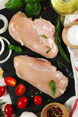 Top view of two raw chicken breasts on a cutting board surrounded by various ingredients