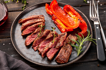 Grilled beef steak, well done with seasons and a glass of red wine on a black wooden background and plate close up