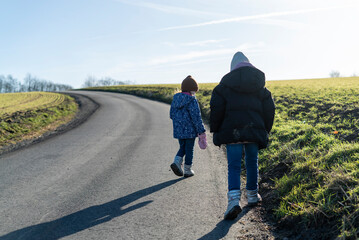 Two little children in warm clothes playing on empty rural asphalt road. Children's entertainment concept
