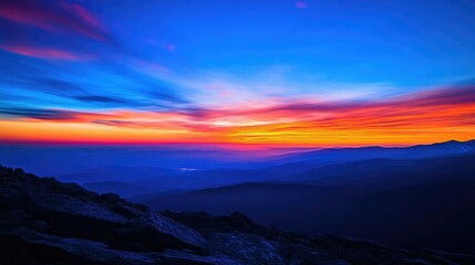 Fototapeta premium A breathtaking sunrise from a mountain summit, with the sky transitioning from deep blue to vibrant orange and pink hues.