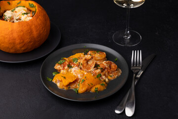 Whole baked pumpkin with tiger prawns, melted cheese, tomatoes and a glass of white wine. Traditional dish of Brazil, home cooking. Selective focus, close-up, black background.