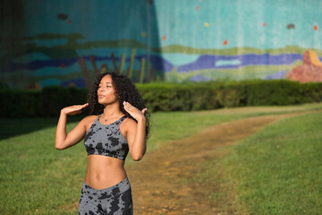 Fototapeta premium Young, pretty, brunette, Latina woman with curly hair and sports clothes, fanning herself with her hands, tired and very hot after completing her exercise routine. Concept sport, exercise, running.