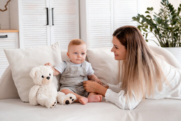 mom with a child, a young mother plays with her little son at home on the couch, maternal love and care, happy decree, mom and a little boy, mom teaches the baby