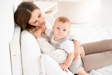 mom with baby, young mom gently hugs and kisses her baby son at home on the bed, maternal love and care, happy decree, mother and little baby boy
