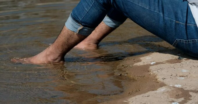 Close up static shot of man lying by river with bare feet in water