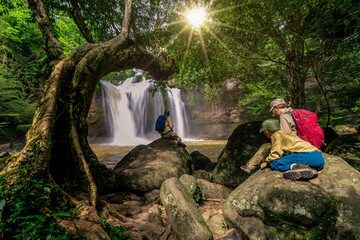 Waterfall in the rainforest on the walkway and family adventurer hiker with backpack standing in front of tropical waterfall Thailand.