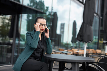 pretty caucasian businesswoman is walking and talking by phone near modern office building