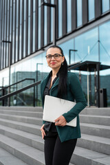 Portrait of a young beautiful woman in suit  standing outside near glass office center