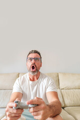 Front View of Excited Middle-Aged Man Enthusiastically Playing Video Games on His Sofa at Home