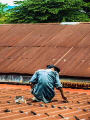 Technician man using polyurethane to seal leak on tiles roof. Man repaired roof by applying sealant...