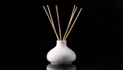 White ceramic diffuser bottle with natural wood reeds, isolated on black background.