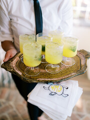 someone holding gold tray of cocktails bright yellow