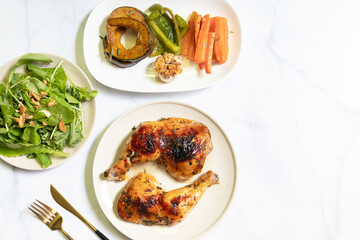 Delicious roasted chicken served with vegetables and fresh salad on a marble table.