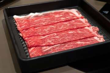 Fresh, thinly sliced beef ready for cooking on a grill.