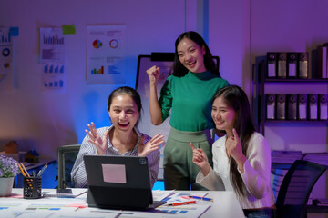 Excited businesswomen celebrating success looking at laptop in office at night