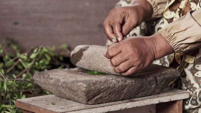 An Asian woman grinds leaves from the henna tree to make henna paste